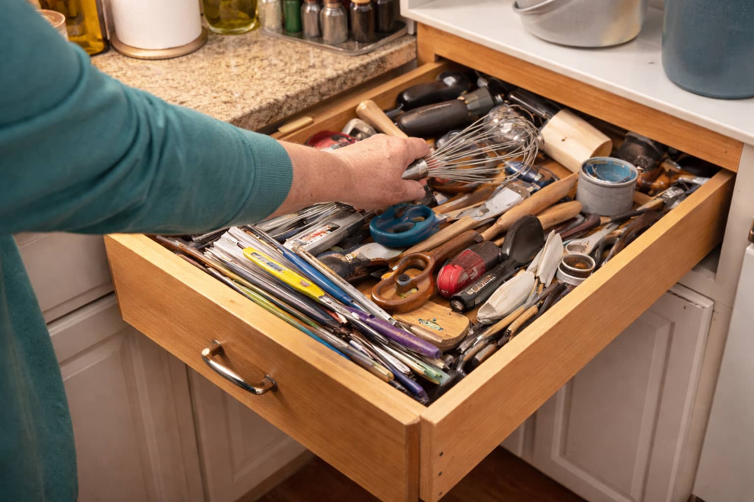 Person reaching into an overstuffed drawer with items shifting